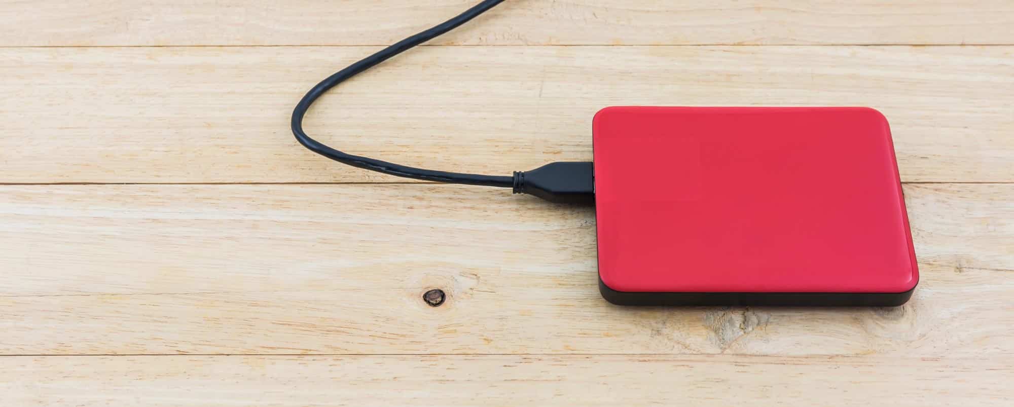 En röd extern hårddisk på ett träbord
