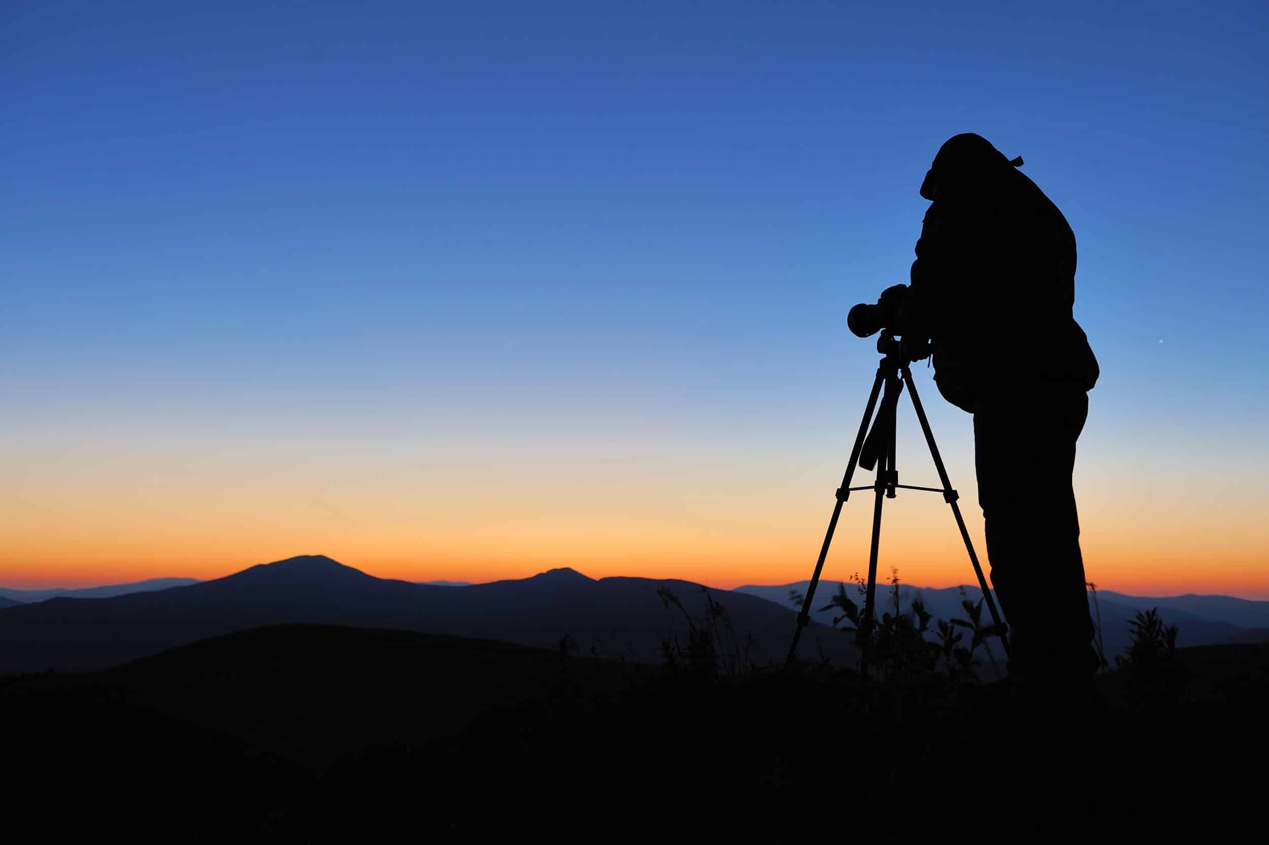 Fotograf bildar siluett när han fotograferar landskap i solnedgång